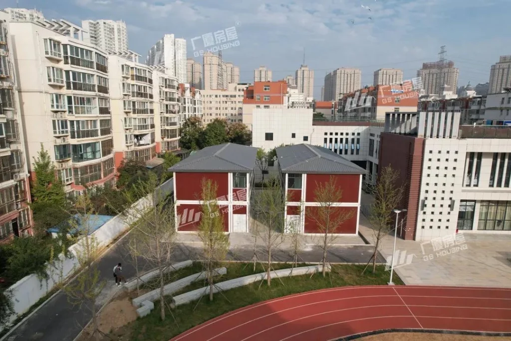 modular school campus building aerial view with red facade classroom blocks and residential buildings background