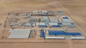 Aerial view of the SDW modular construction camp in Saudi Arabia, showing separate functional zones including blue-roof office buildings, rows of white prefabricated steel accommodation blocks, internal access roads and shared facilities within a fenced desert compound