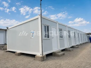 Close-up view of horizontally connected flat pack container house modules at the Uganda project site, showing structural corner posts, unit connection joints, security-barred windows and concrete step access