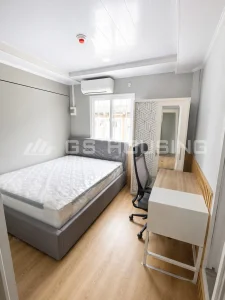 Completed interior of a modular dormitory bedroom at the Indonesia workforce accommodation project, showing a double bed, desk with office chair, wardrobe with mirror, air conditioning unit, smoke detector and wood-look flooring