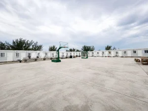 Completed modular construction site accommodation units arranged around a central outdoor area at the Bahamas stadium renovation project, with paved access space, basketball courts and shared facilities