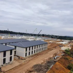 Elevated view of IPIP mining camp construction site showing completed dormitory buildings in foreground and cranes assembling modular units in background