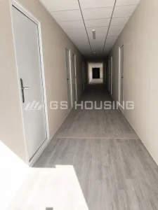 Interior corridor in the client office zone at the SDW modular construction camp in Saudi Arabia, showing rows of frosted-glass office doors, suspended ceiling with LED lighting, finished wall panels and grey flooring, with natural light at the far end