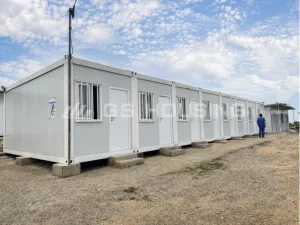 Long row of single-storey flat pack container house units connected horizontally on concrete footings at the Uganda construction site accommodation, with security-barred windows and step access to each unit