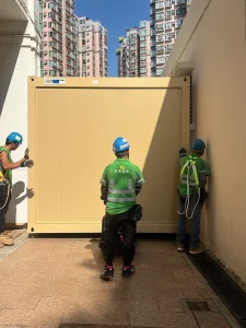 Workers moving a prefabricated modular classroom unit through a restricted passage at a Tai Po school site