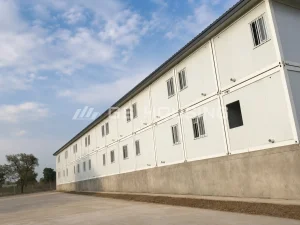 Low-angle side view of the two-storey office building at the 2024 Mali project, showing rows of barred windows across both floors, concrete base, visible container module joints and a paved access area alongside the building
