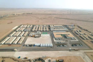 Large modular camp with organized building rows, internal roads and fenced perimeter in a desert site