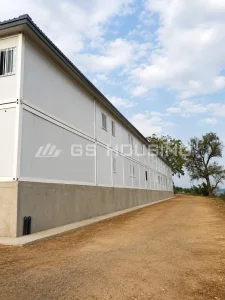 Side view of the two-storey office building at the 2024 Mali project, showing individual container modules joined together, concrete base, barred windows and a dirt road alongside trees