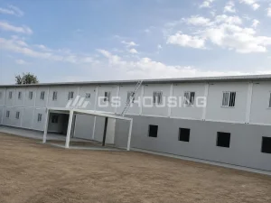 Two-storey office building at the 2024 Mali project, with a covered entrance area, metal access ladder, paved walkway and sandy ground under a partly cloudy sky