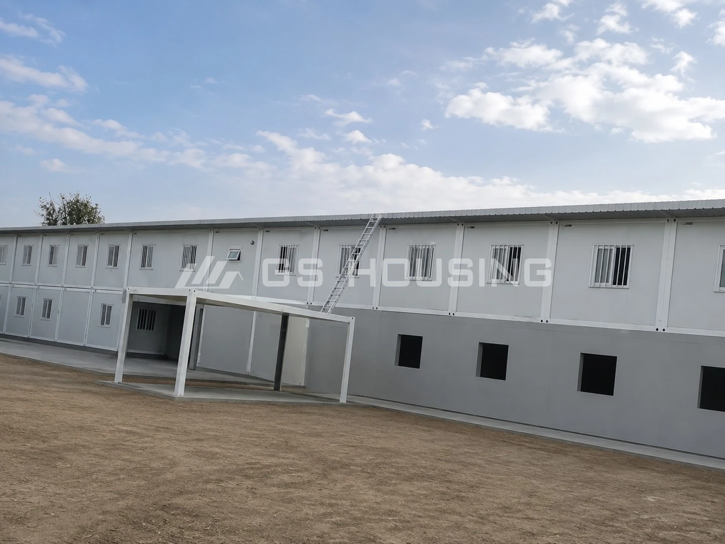 Two-storey office building at the 2024 Mali project, with a covered entrance area, metal access ladder, paved walkway and sandy ground under a partly cloudy sky