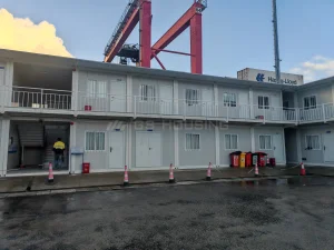 Two-storey prefabricated site building at the Guinea Conakry port project, with external stairs, covered walkways, container terminal equipment and a shipping container in the background